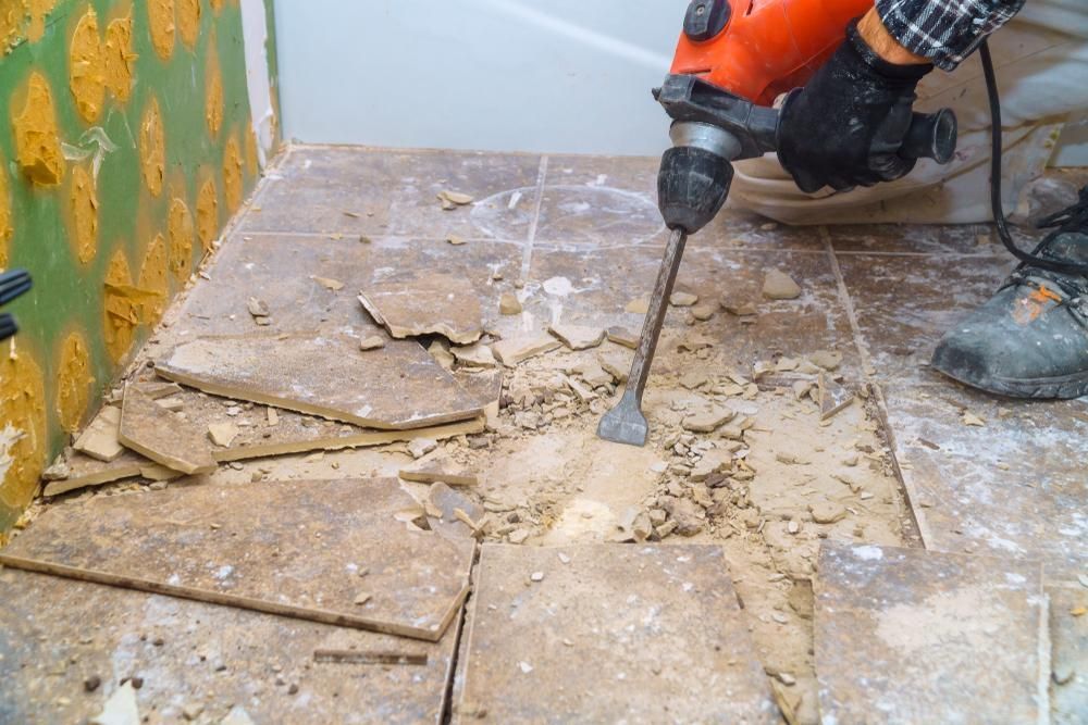a Person is Using a Hammer Drill to Remove Tiles From the Floor — Port Stephens Bathrooms In Nelson Bay, NSW