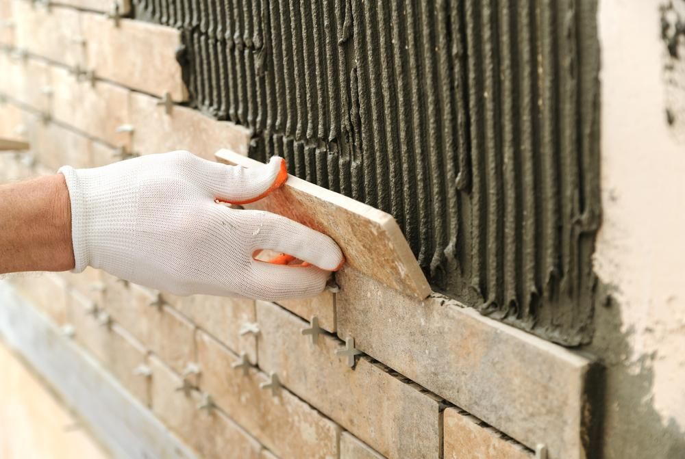 a Person is Laying Tiles on a Brick Wall — Port Stephens Bathrooms In Nelson Bay, NSW