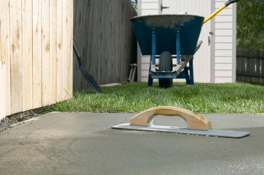 a Trowel is Laying on a Concrete Surface Next to a Wheelbarrow — Port Stephens Bathrooms In Nelson Bay, NSW