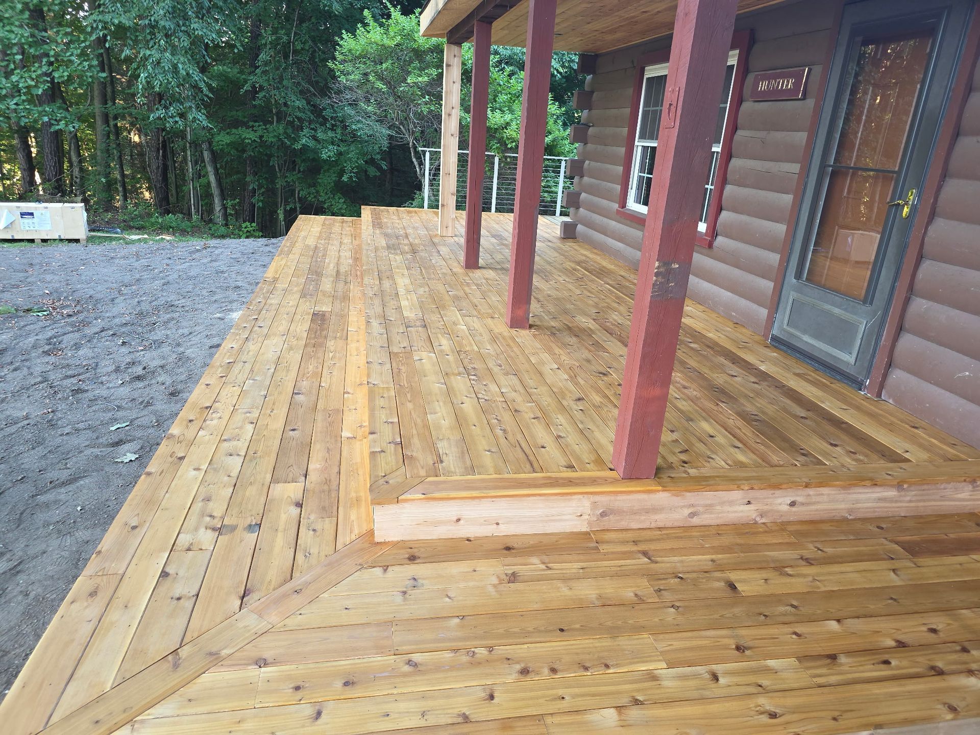 Wooden deck and ramp beside a cabin, with red support posts and gravel yard.