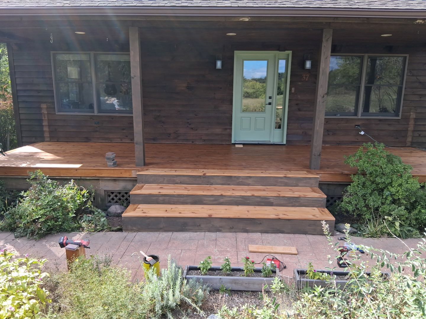 Wooden front porch with steps, a white door, windows, and flower beds in front