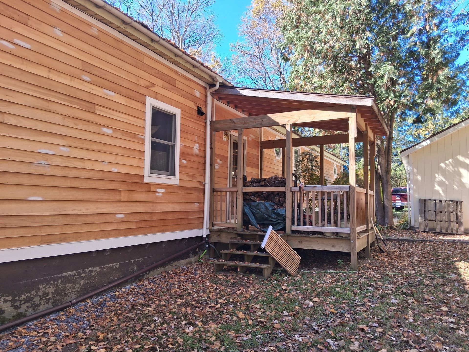 Wooden house with a small porch and steps, surrounded by fallen leaves and trees.