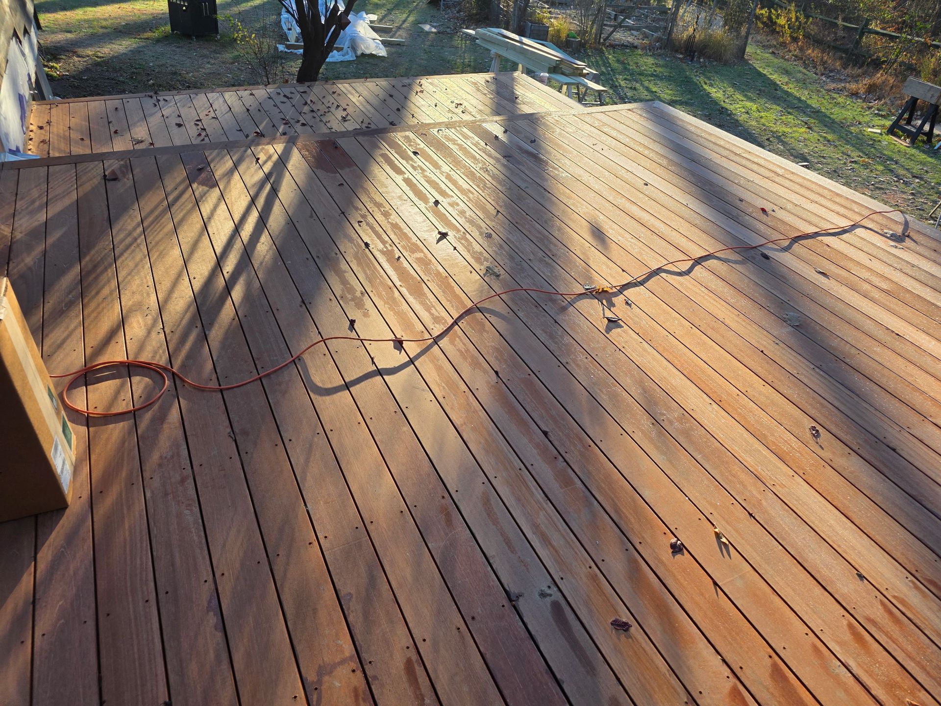 Wooden deck under construction with loose black cable and tools in sunlight near trees