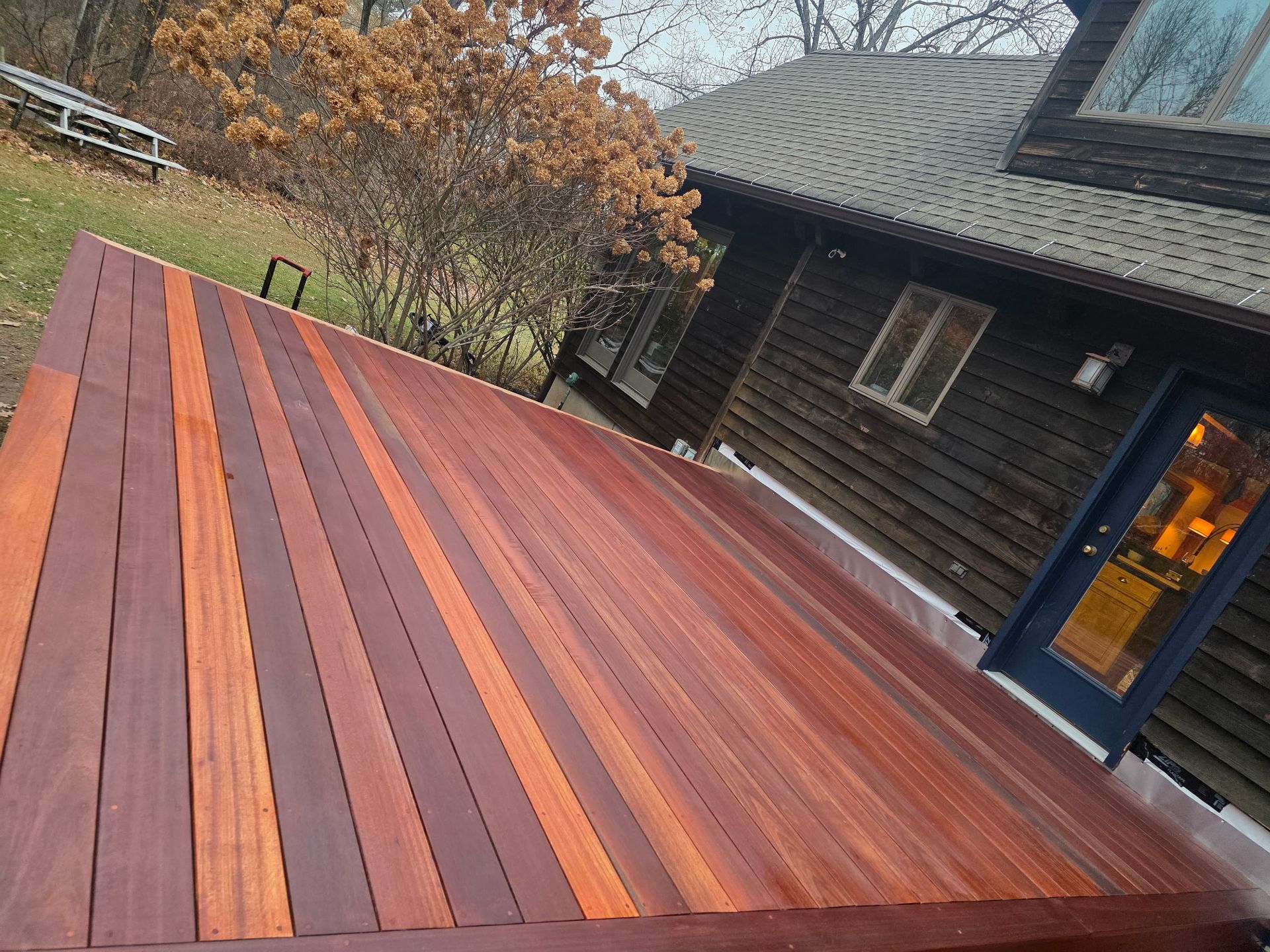 Wooden deck with dark and orange planks beside a log cabin and trees in autumn