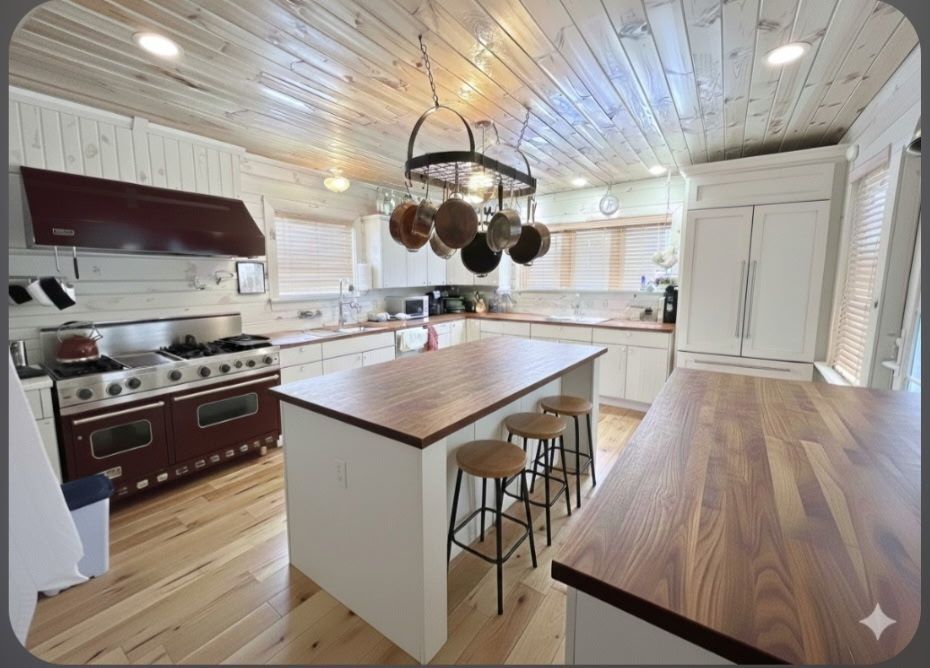 Bright, modern kitchen with wood countertops, white cabinets, red stove, and central island with stools
