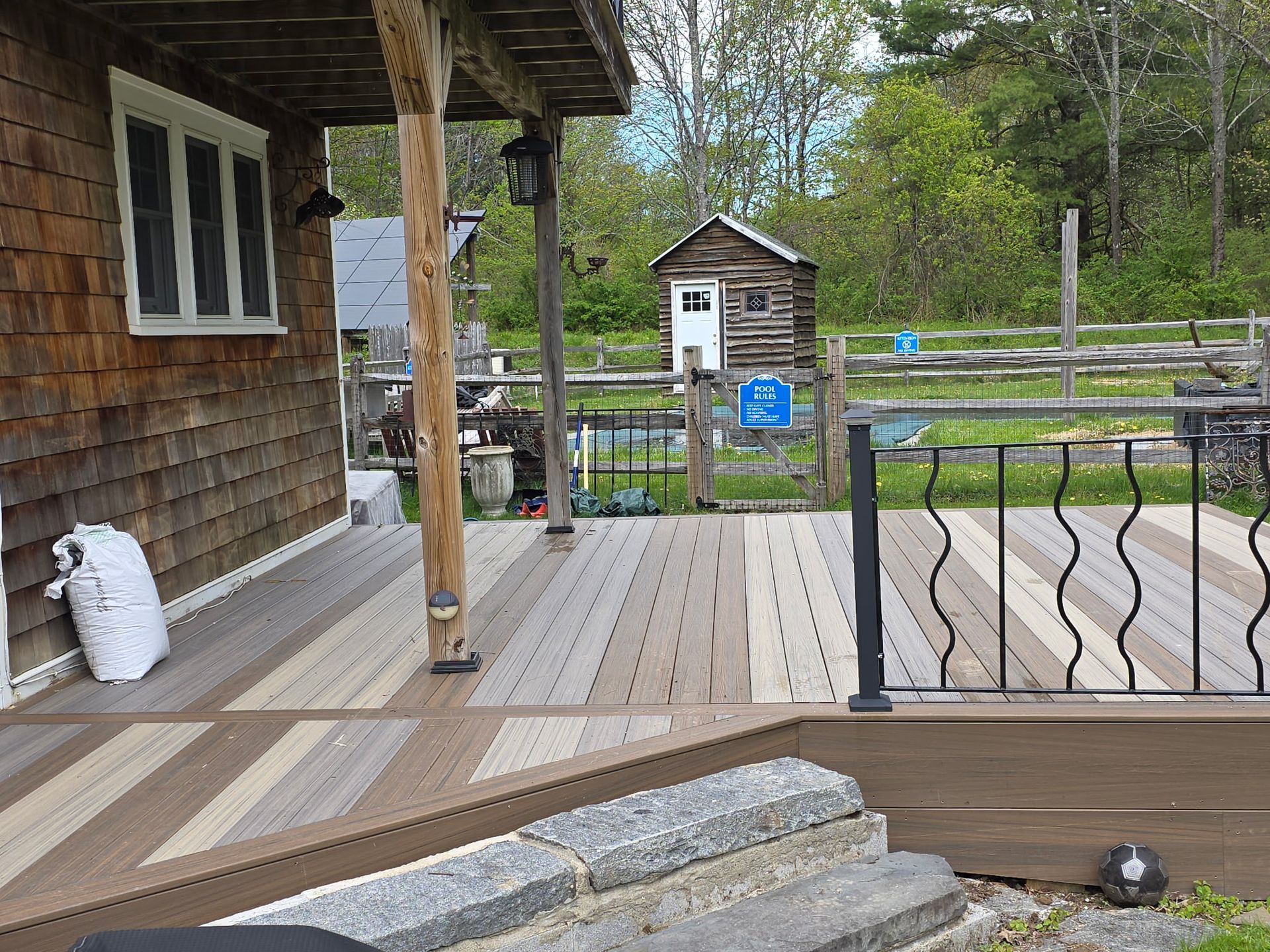 Wooden porch with white windows, steps, a railing, and a view of a yard and small shed beyond.