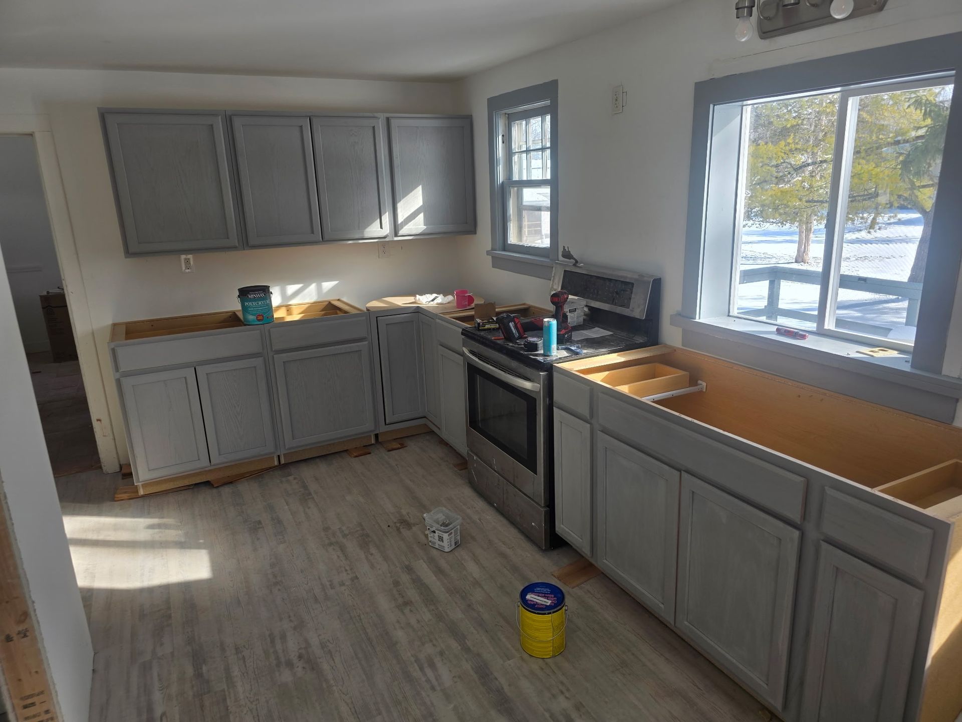 Small kitchen with gray cabinets, wood countertops, stove, sink, and sunlight through a window.