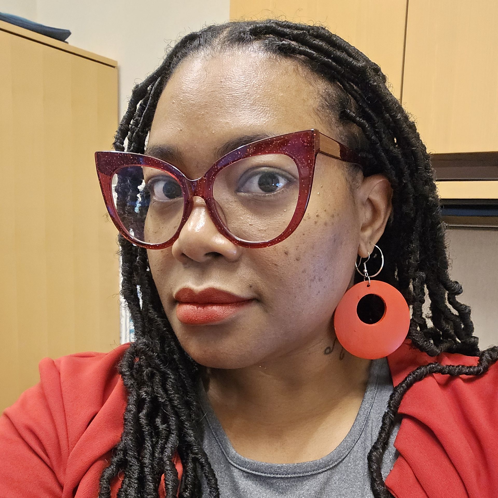 A woman wearing glasses and earrings is looking at the camera.