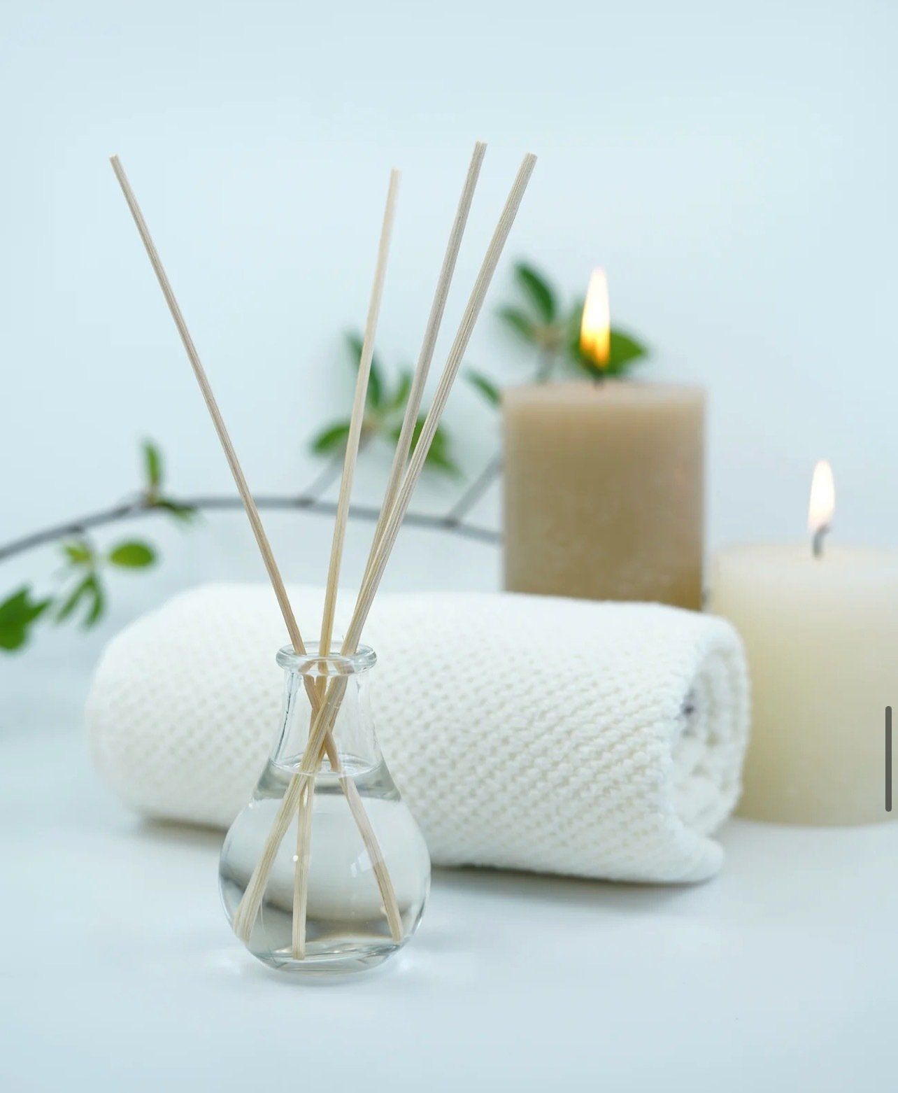 A small bottle of reed diffusers sits next to a towel and candles