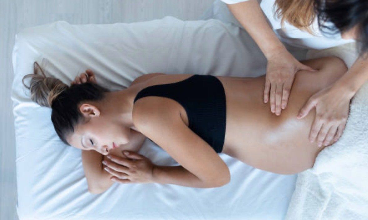 A pregnant woman is laying on a bed getting a massage.