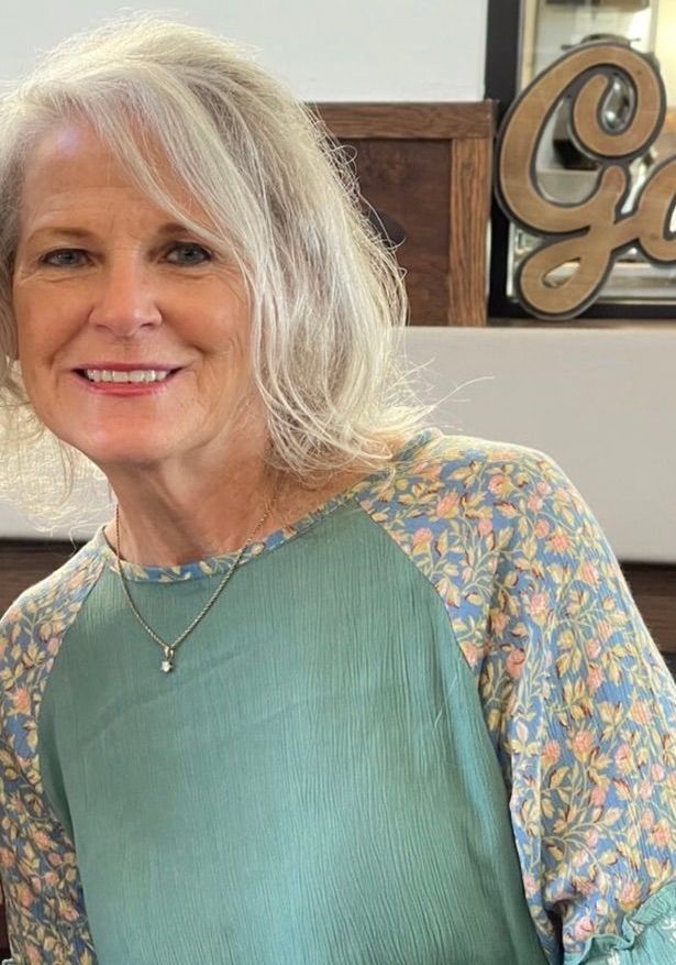A woman wearing a green sweater and a necklace is smiling.