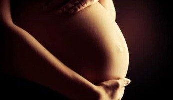 A pregnant woman is holding her belly with her hands.