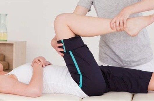 A man is stretching a woman 's leg on a table