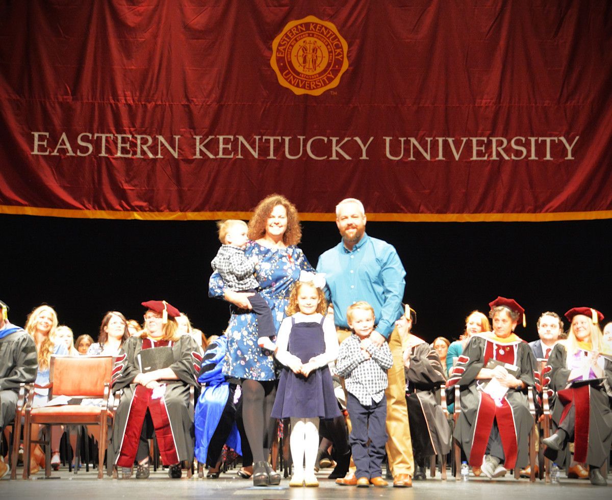 Family poses on stage at Eastern Kentucky University graduation. Banner in background.