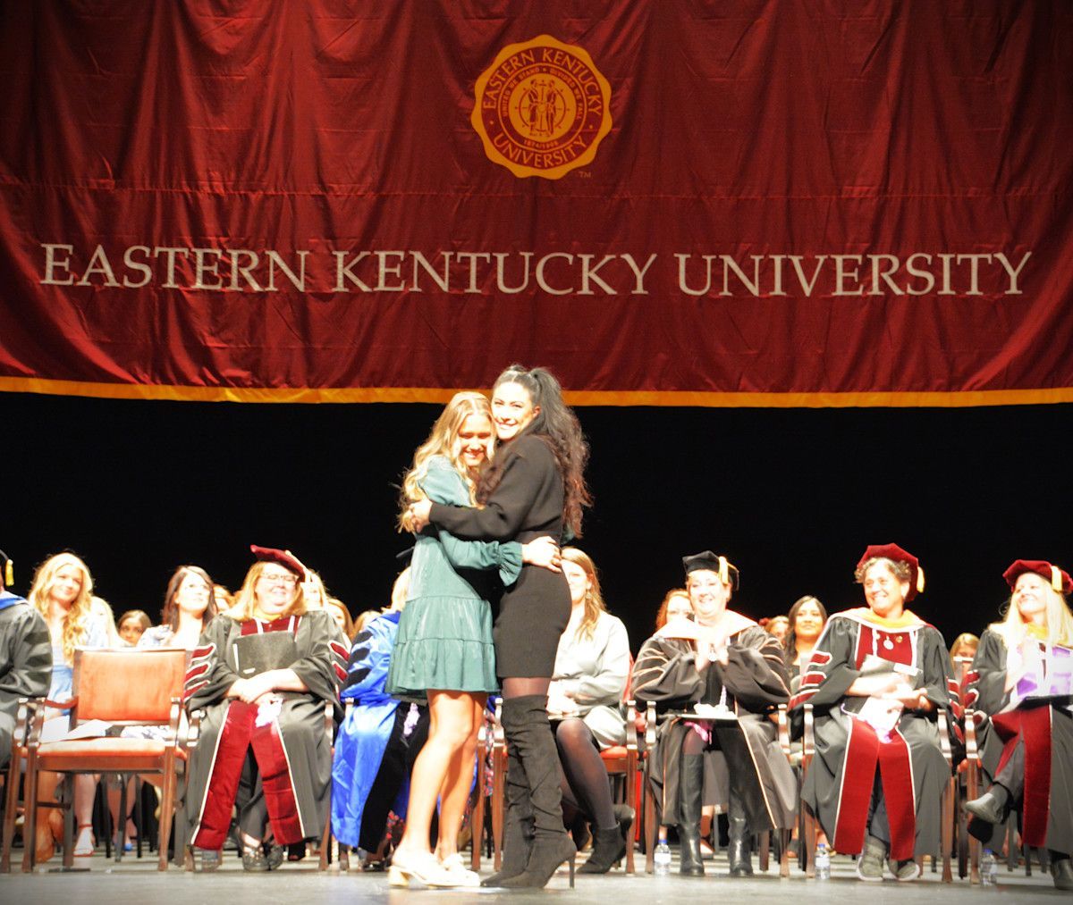 Two women hugging on stage at Eastern Kentucky University graduation.