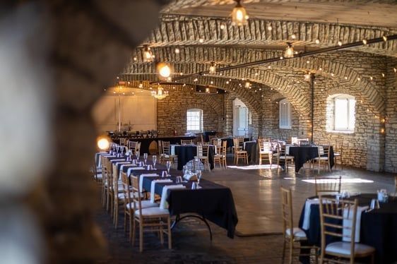 Interior of a stone-walled event space set up with tables, chairs, and string lights.