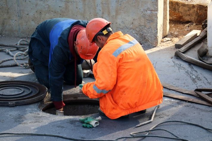Two Construction Workers Are Working On A Manhole Cover — Cool & Secure In Noosa, QLD