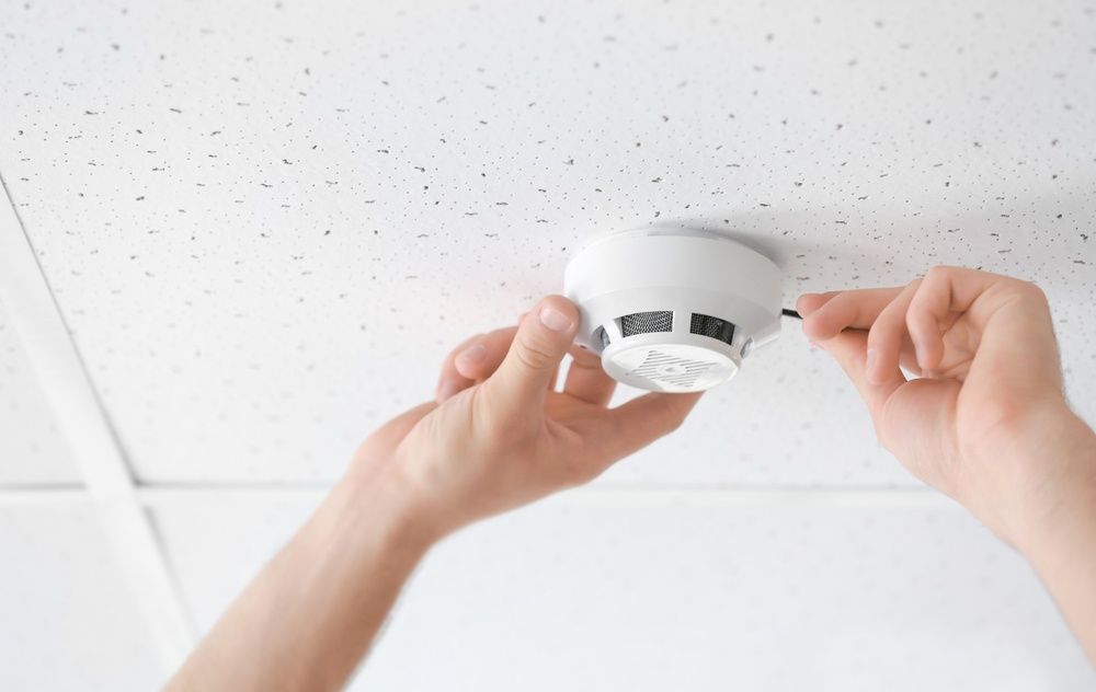 A Person Is Installing A Fire Alarm On The Ceiling — Cool & Secure In Buderim, QLD