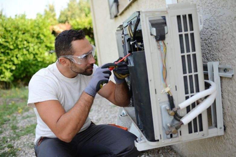 A Man Is Working On An Air Conditioner Outside Of A Building — Cool & Secure In Buderim, QLD