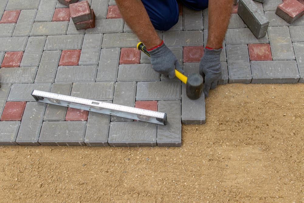 A Man is Laying Bricks on a Sidewalk With a Hammer and a Level — Lennox Build In Lismore, NSW