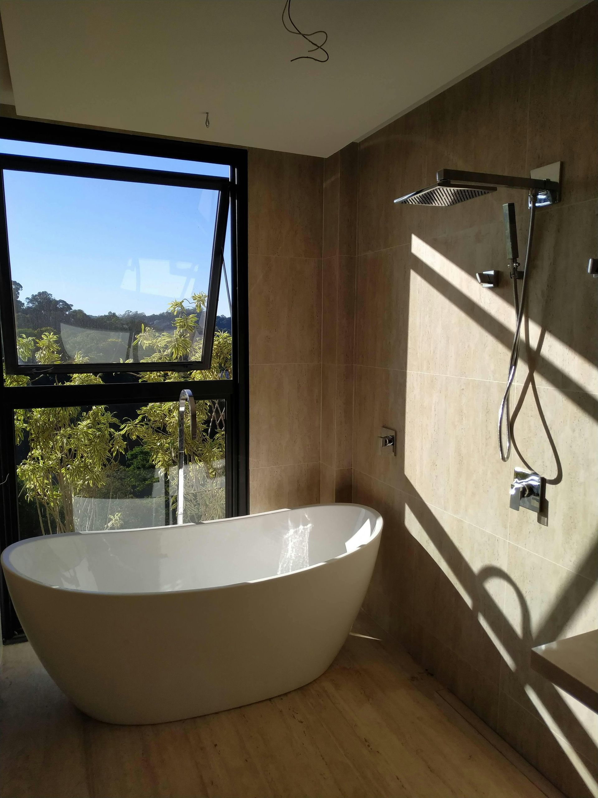 Bathroom with a white freestanding tub, large window, and shower fixtures on a textured wall.