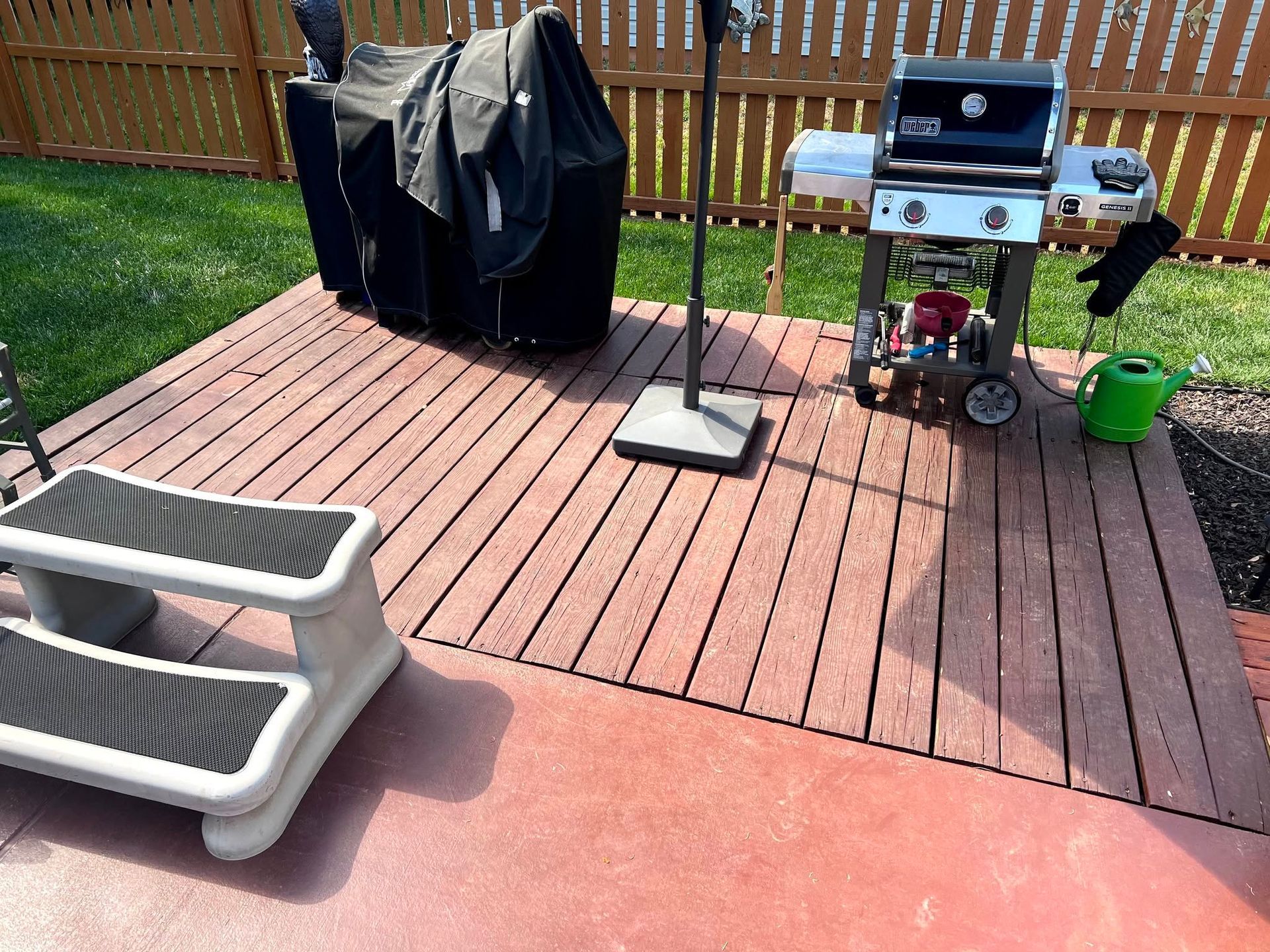 Backyard deck with a grill, covered patio heater, and two planters on a wooden fence patio.