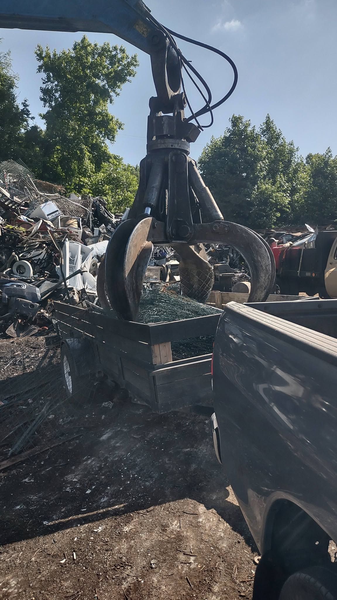 Hydraulic claw loading scrap metal into a truck under bright daylight