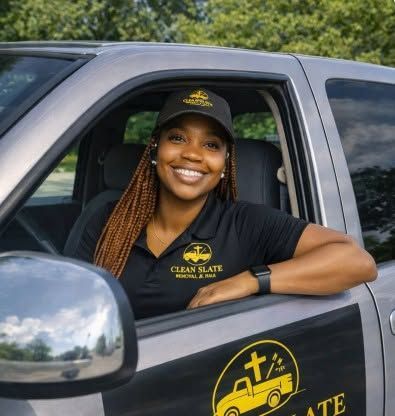 Smiling worker in black polo and cap leaning from gray truck with Clean State logo