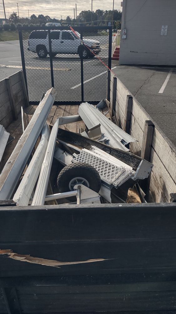 Dumped metal debris and a wheel in a black dumpster beside a chain-link fence in a parking lot.
