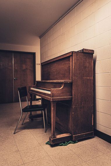 An upright piano with a chair in a small beige room, near a closed wooden door.