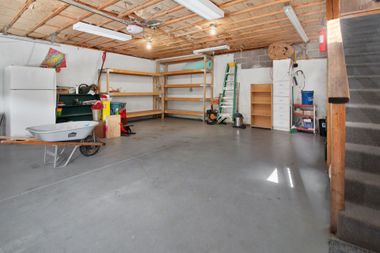 Empty garage with concrete floor, wooden ceiling, shelves, storage items, and a wheelbarrow