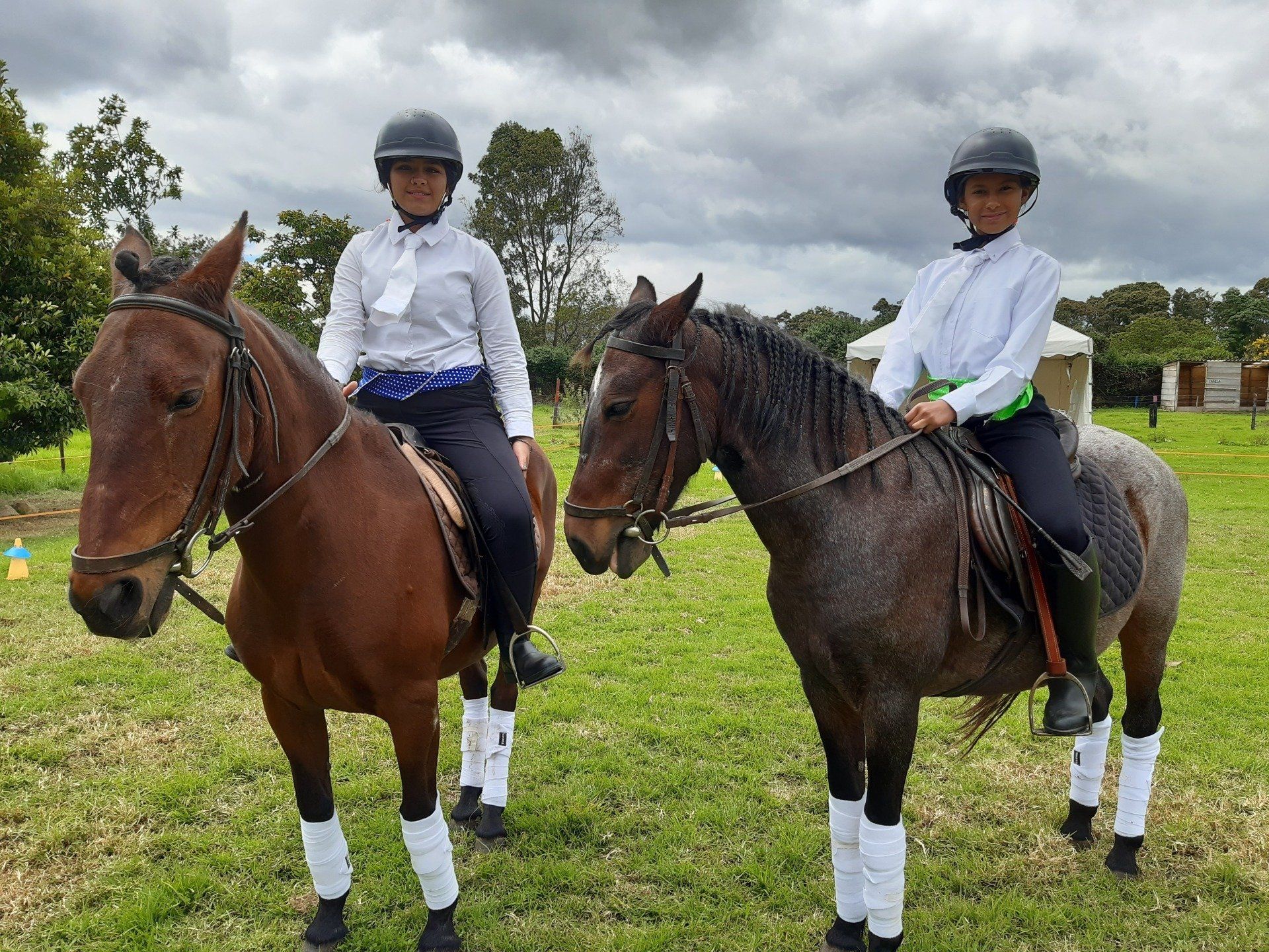 Dos jinetes a caballo en un campo de hierba, con cascos y camisas blancas.