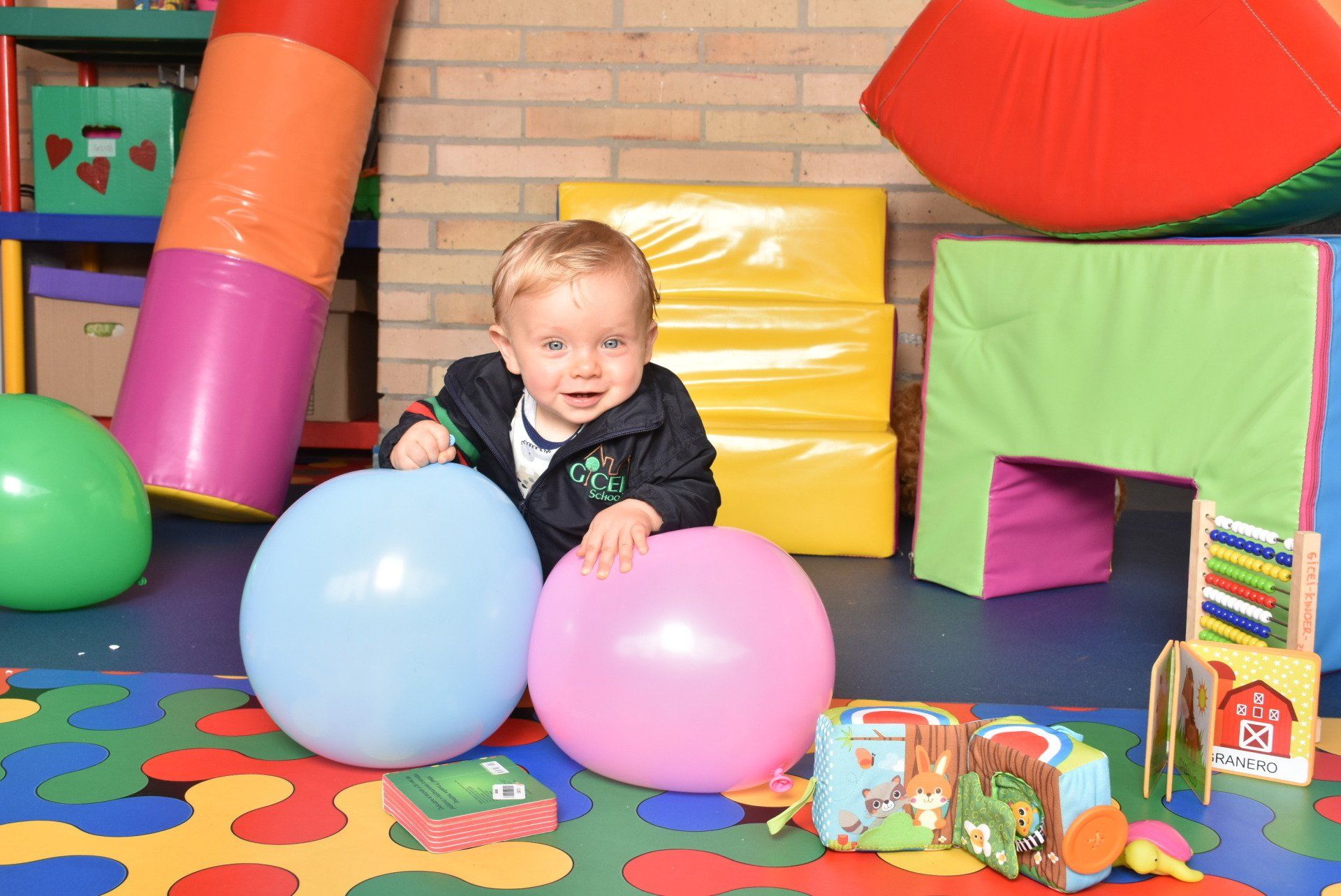 Un niño pequeño juega con globos azules y rosas en una colorida zona de juegos interior.