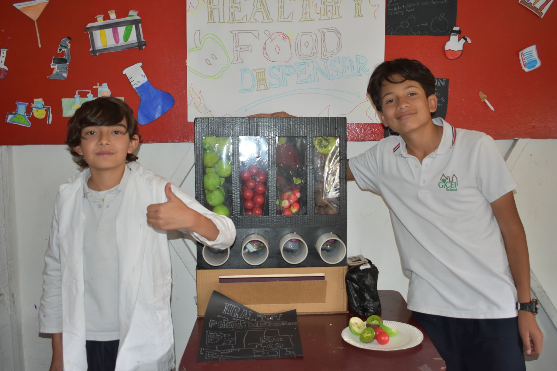 Dos personas posando junto a una exposición de un proyecto científico, sonriendo y levantando el pulgar.