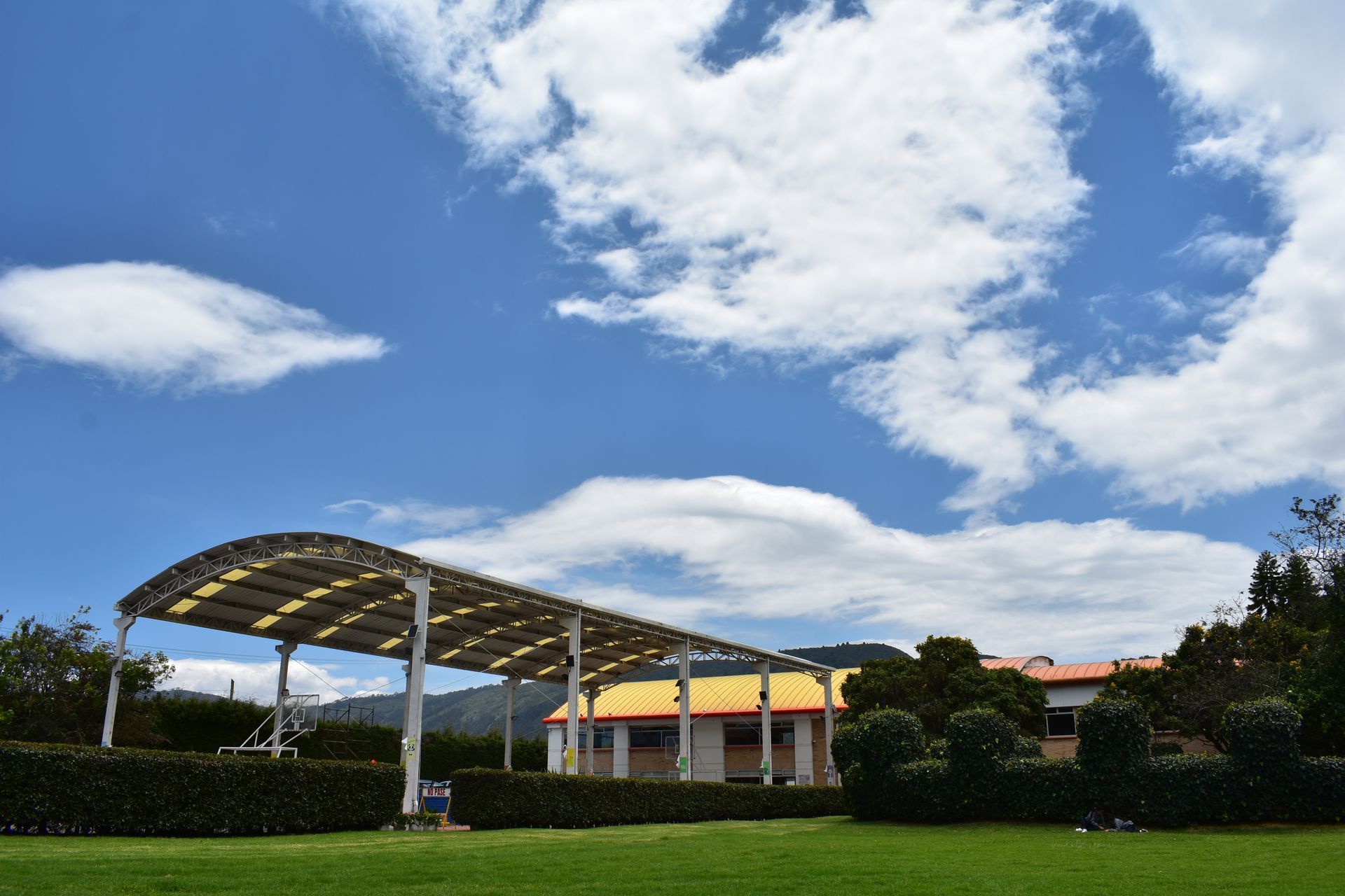Cochera alimentada por energía solar con paneles solares sobre un campo de hierba bajo un cielo azul brillante.