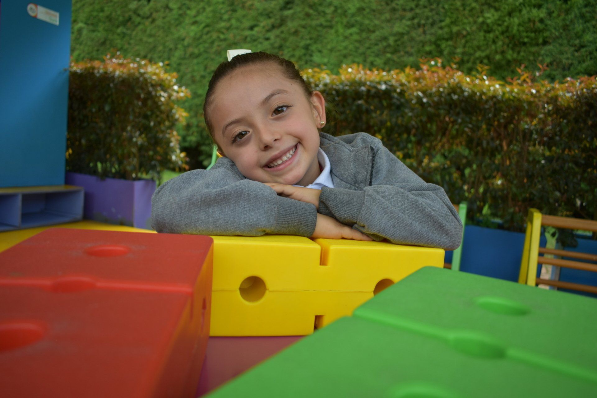 Un niño sonriente se apoya en bloques de colores al aire libre en un parque infantil con césped.