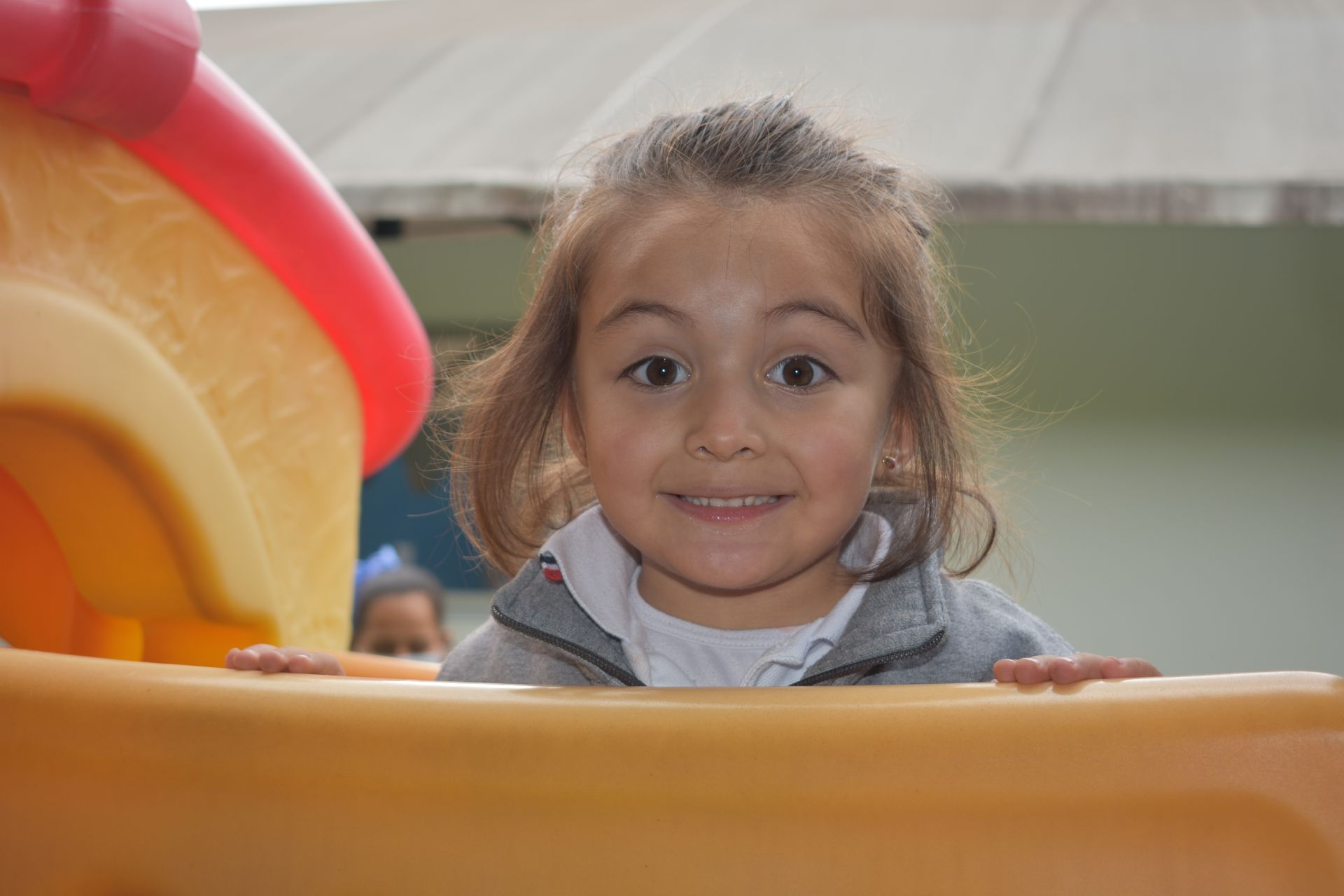 Un niño sonríe en un tobogán de un parque infantil, asomándose por el borde naranja.