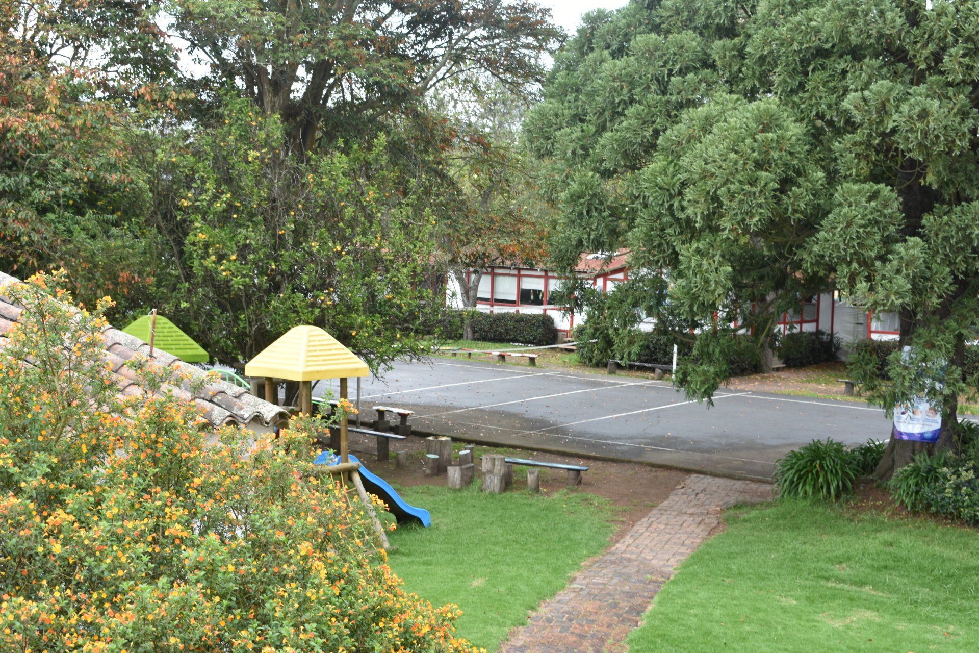 Parque con sendero serpenteante, árboles, tobogán infantil y sombrillas amarillas bajo un cielo gris.