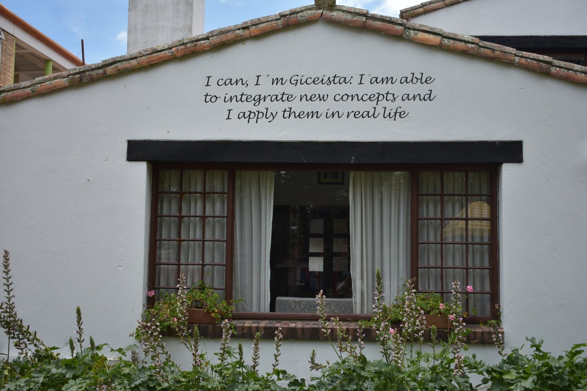 Fachada blanca con toldo negro, ventana con barrotes y letrero sobre la entrada.