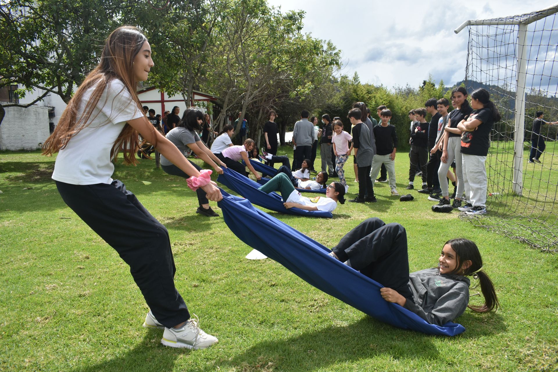 Dos personas tiran de un cabestrillo azul en un parque con césped mientras otras observan cerca.