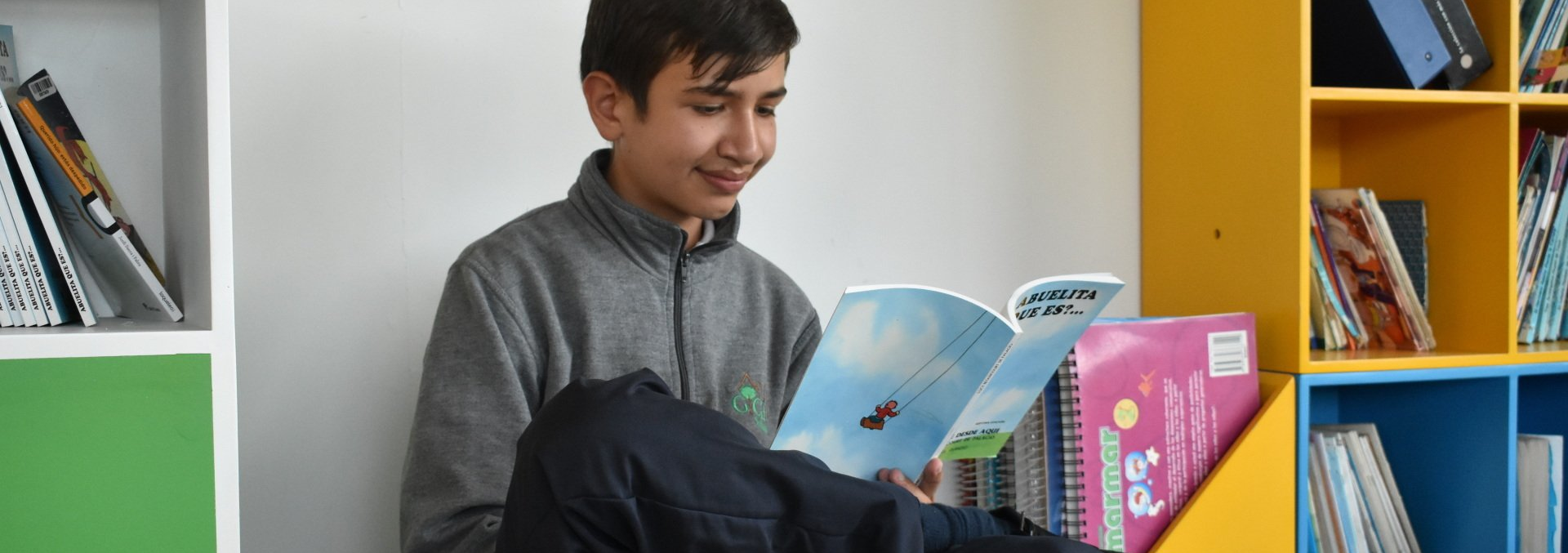 Una persona sonríe mientras lee un libro en un rincón colorido de la biblioteca.