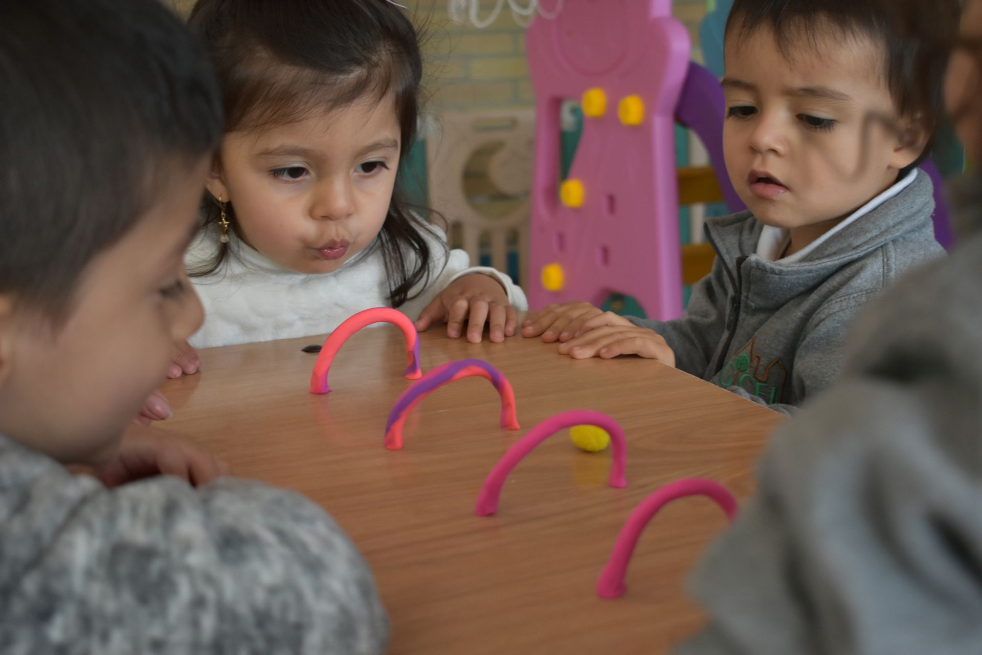 Niños jugando a lanzar aros en una mesa con arcos rosas y expresiones concentradas.