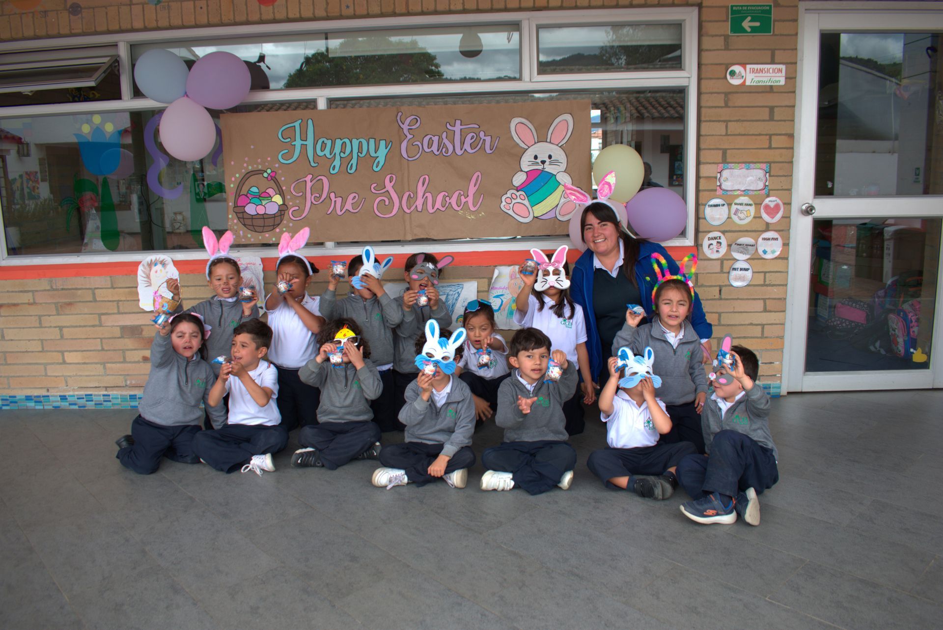 Niños posando frente a un aula con globos y un cartel de 