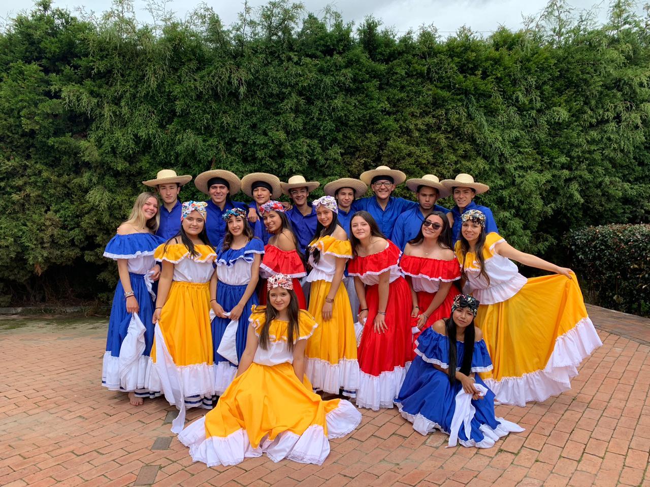 Grupo de personas con coloridos trajes folclóricos posando al aire libre frente a un seto.