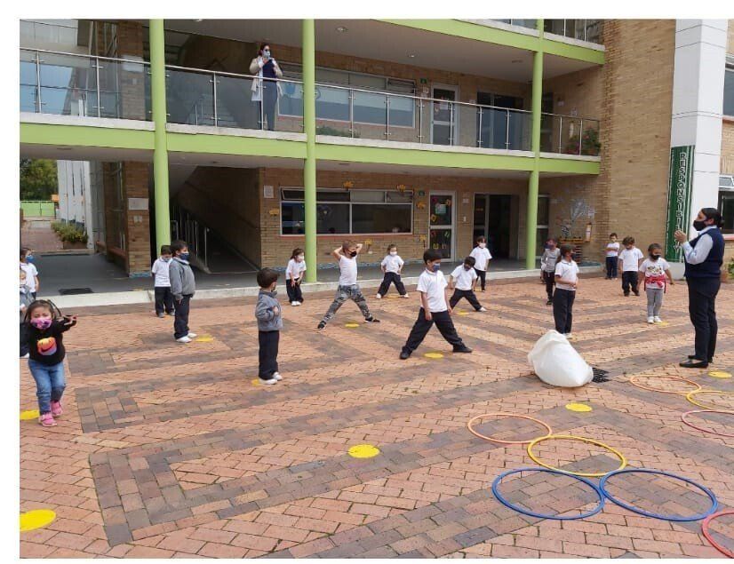 Niños jugando en el patio de una escuela con conos y aros sobre una superficie pavimentada con ladrillos.