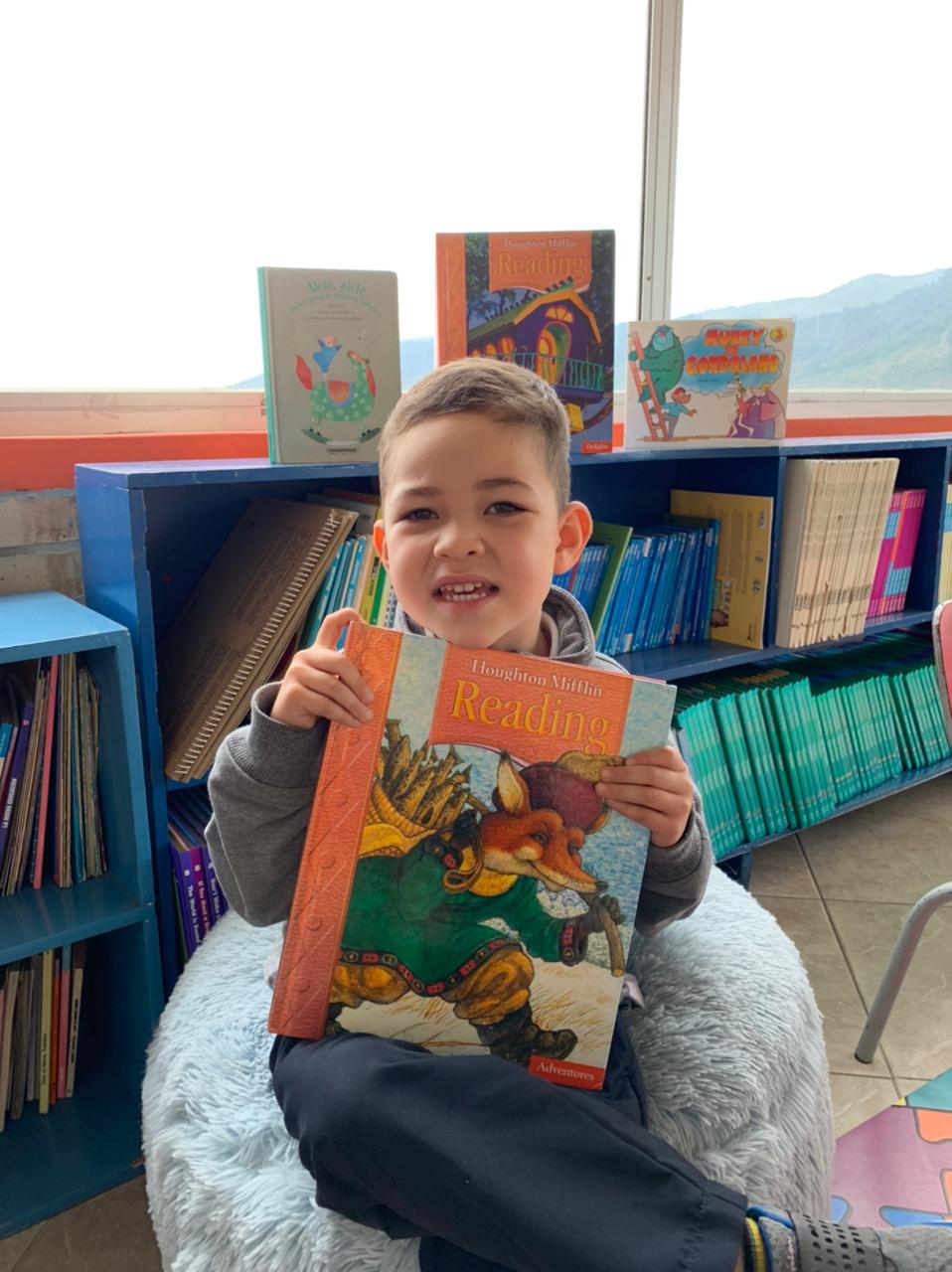 Un niño sentado en una silla mullida sostiene un colorido mosaico frente a una estantería.