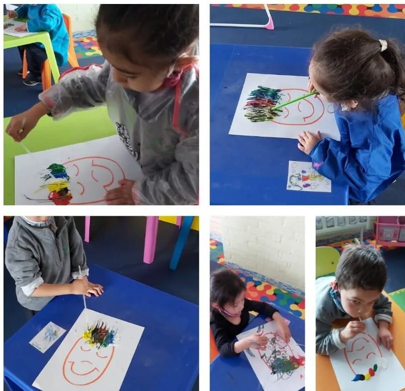 En una colorida actividad manual en el aula, los niños dibujan caras con pintura sobre papel.
