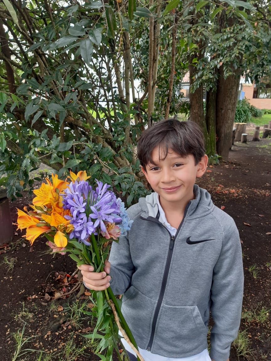 Una persona sostiene un ramo de flores naranjas y moradas en un jardín y sonríe a la cámara.