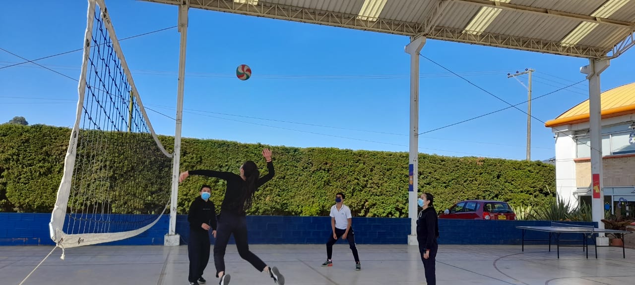 Gente jugando al voleibol en una cancha al aire libre bajo un cielo azul despejado.