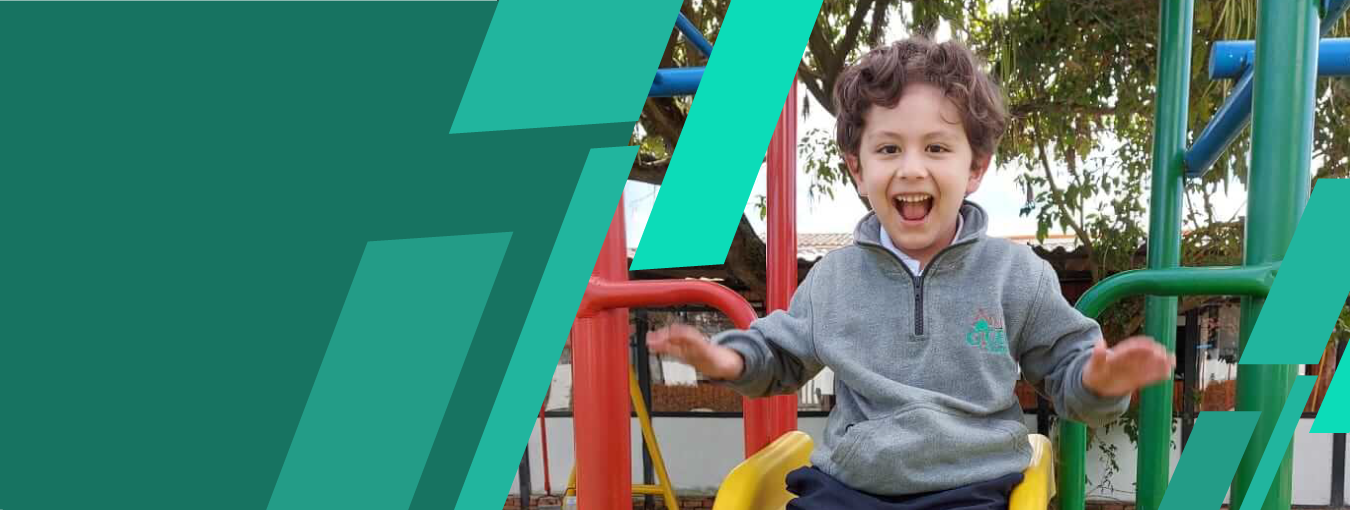 Un niño sonríe en un columpio de un parque infantil, lleva una sudadera gris con capucha y, de fondo, hay juegos infantiles verdes.